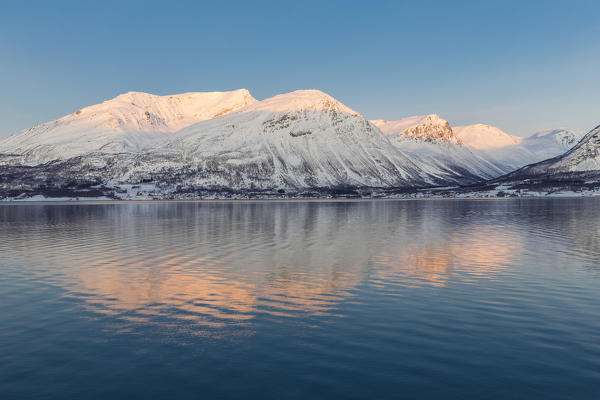 The peaks illuminated by the setting sun are reflected in Kafjorden. Kafjorden, Lyngen Alps, Troms, Norway, Lapland, Europe.