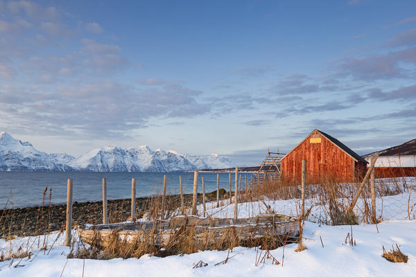 An old boat and red fishermen's houses overlooking the fjord. Nordmannvik, Kafjord, Lyngen Alps, Troms, Norway, Lapland, Europe.