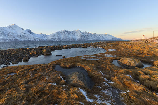 The sun illuminates the coast near a traditional lighthouse. Spaknesora naturreservat, Djupvik, Lyngenfjord, Lyngen Alps, Troms, Norway, Lapland, Europe.