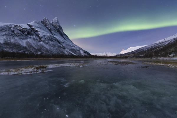 Otertinden, one of the mythical peaks of Norwegian Lapland with the northern lights that colored green ice of a pond. Otertinden, Signaldalen, Storfjord, Lyngen Alps, Troms, Norway, Lapland, Europe.