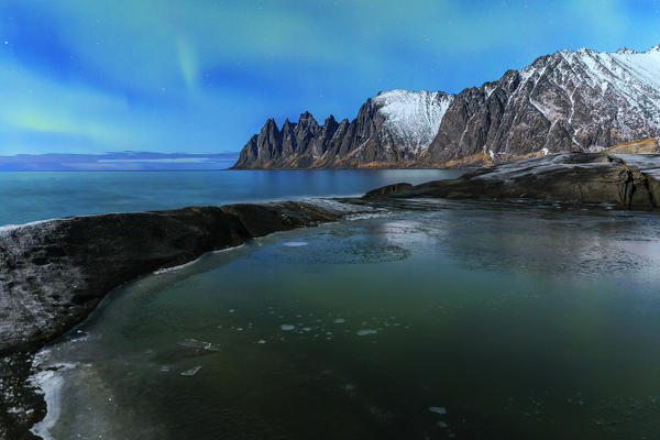 A weak nothern lights reflects in an icy puddle. Tungeneset, Ersfjorden, Senja, Norway, Europe.