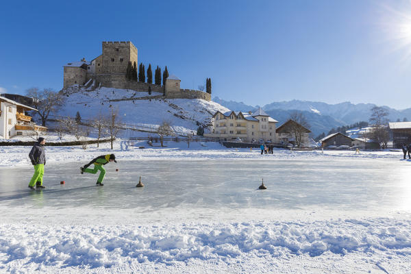 Boys play curling on the frozen pond at the foot of Ladis Castle. Ladis, Inntal, Tirol, Osterreich, Europe