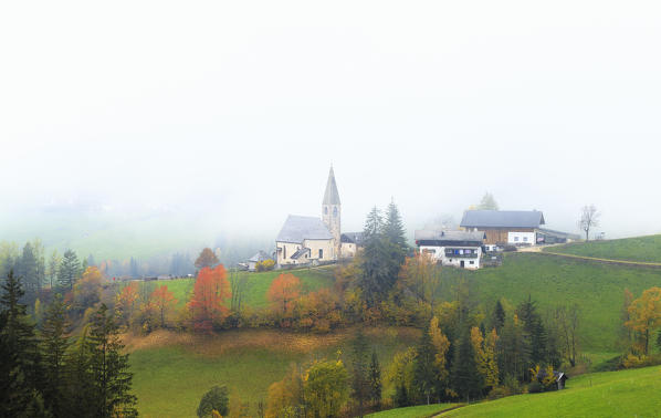 Church of Santa Magdalena in the autumn mist. Funes Valley, South Tyrol, Dolomites, Italy