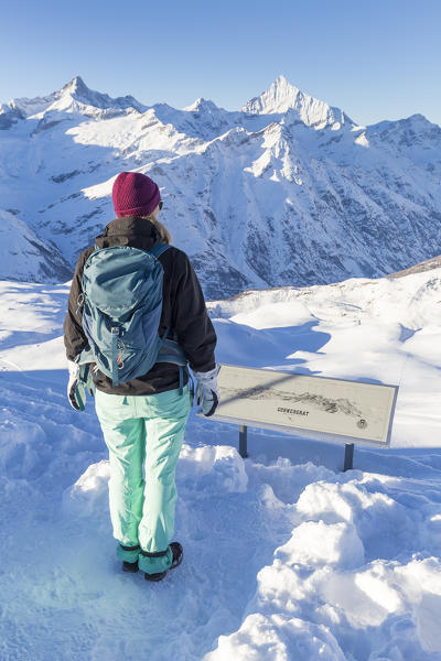 Tourist is reading an informative map at the viewpoint of Gornergrat facing the snowy peak of Dent Blanche and Weisshorn.  Gornergrat, Zermatt, Canton of Valais / Wallis, Switzerland.
