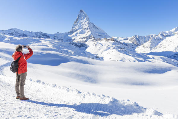 A tourist take a photo with his smartphone in front of Matterhorn. Riffelberg, Zermatt, Canton of Valais / Wallis, Switzerland.
