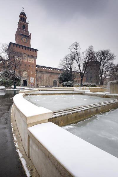 A iced fountain and Sforzesco Castle after a snowfall. Milan, Lombardy, Northern Italy, Italy.