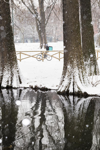 Cyclist walks through the Sempione Park during a snowfall. Milan, Lombardy, Northern Italy, Italy.