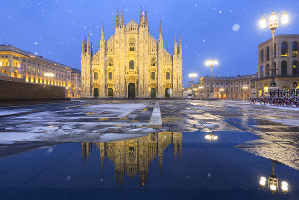 Duomo of Milan is reflected in a puddle during a snowfall at twilight. Milan, Lombardy, Northern Italy, Italy.