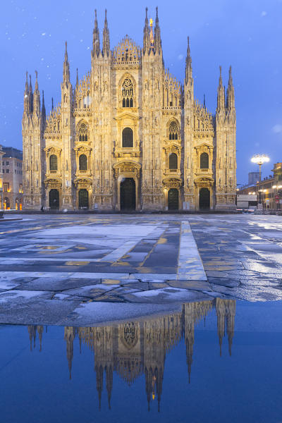 Duomo of Milan  is reflected in a puddle during a snowfall at twilight. Milan, Lombardy, Northern Italy, Italy.