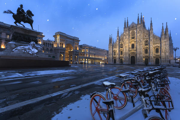 Bicycles parked in PIazza Duomo during snowfall at dusk. Milan, Lombardy, Northern Italy, Italy.
