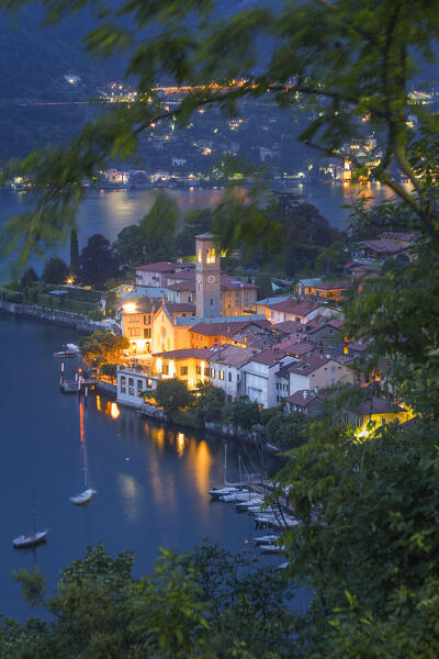 Trees frame the Nesso village illuminate at Dusk, lake Como, Como province, Lombardy, Italy, Europe