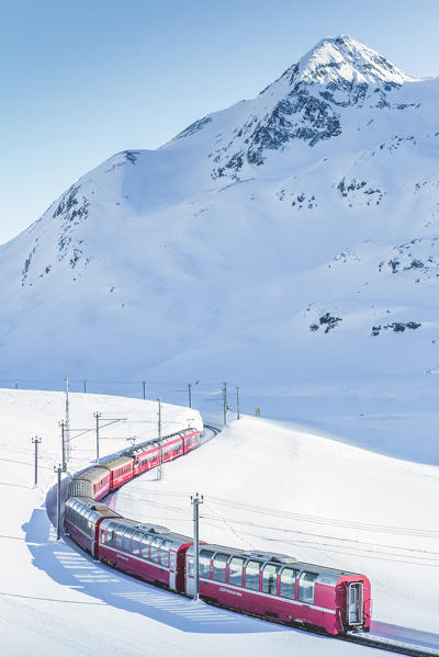 Bernina Express red train passing Lago Bianco in a scenic winter mountain landscape, Graubunden, Switzerland