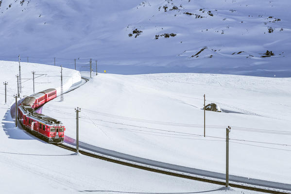 Bernina Express red train passing Lago Bianco in a scenic winter mountain landscape, Graubunden, Switzerland