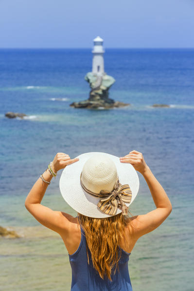 Close up of a young woman with a straw hat admiring the enchanting offshore Tourlitis lighthouse in the background, Andros, Cyclades Archipelago, Greece, Europe