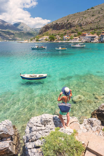 Young woman with a straw hat and a turquoise dress admiring the turquoise sea at Limeni, Mani region, Peloponnese, Greece, Europe