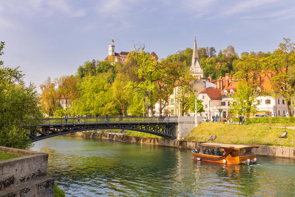 Touristic boat on Ljubljanica river near Hradecky Bridge and the iconic medieval Ljubljiana castle in the background. Ljubljiana, Osrednjeslovenska, Slovenia
