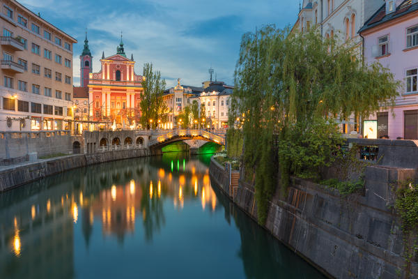 Old town and triple bridge reflected on Ljubljanica river and Franciscan church of Annunciation in the background. Ljubljiana, Osrednjeslovenska, Slovenia