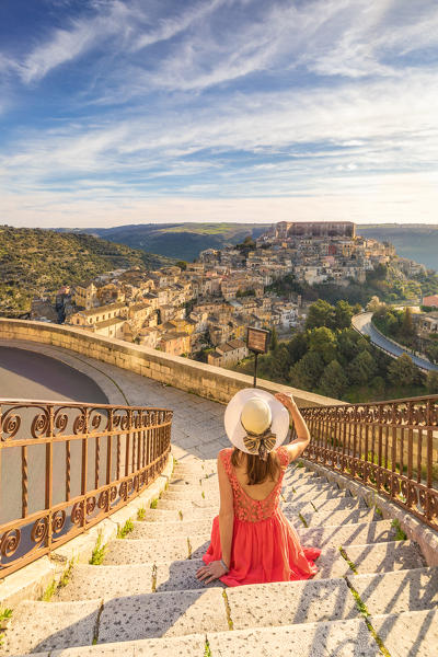Young woman admiring the enchanting hilltop city of Ragusa Ibla from the stairs of Santa maria delle Scale church, Ragusa, Sicily, Italy  (MR)