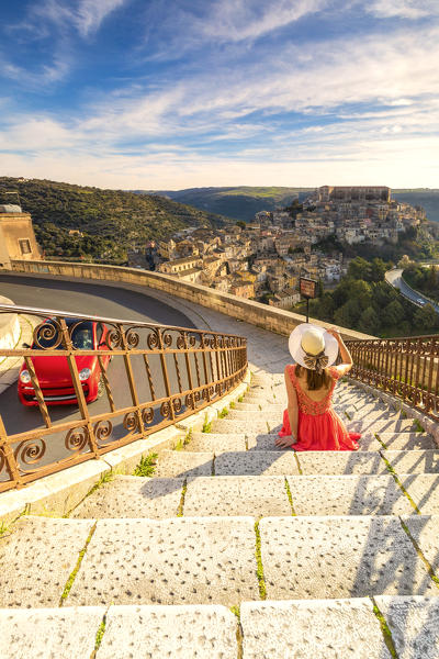 Young woman admiring the enchanting hilltop city of Ragusa Ibla from the stairs of Santa maria delle Scale church, Ragusa, Sicily, Italy