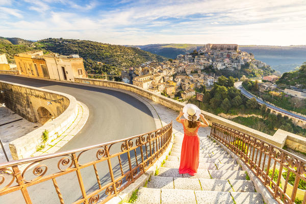 Young woman admiring the enchanting hilltop city of Ragusa Ibla from the stairs of Santa maria delle Scale church, Ragusa, Sicily, Italy