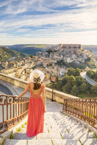 Young woman admiring the enchanting hilltop city of Ragusa Ibla from the stairs of Santa maria delle Scale church, Ragusa, Sicily, Italy  (MR)