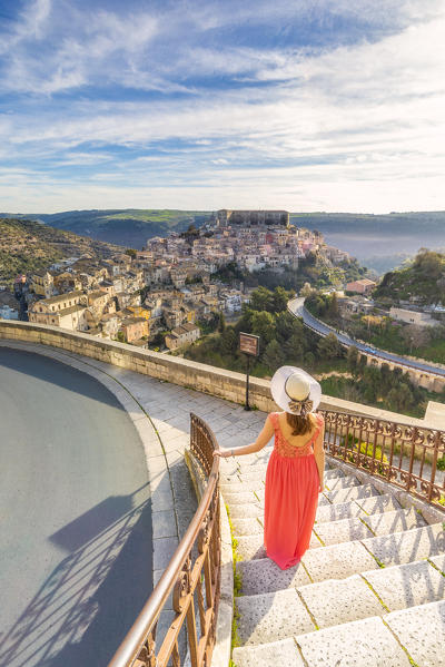 Young woman admiring the enchanting hilltop city of Ragusa Ibla from the stairs of Santa maria delle Scale church, Ragusa, Sicily, Italy