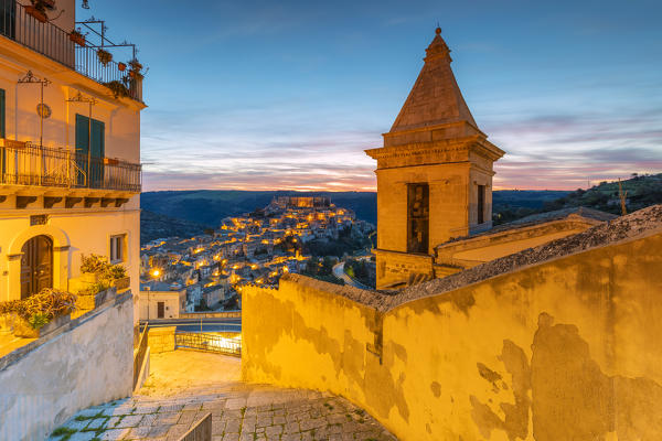 Close up of the bell tower of Santa Maria delle scale church and Ragusa Ibla in the background at sunrise, Ragusa, Sicily, Italy