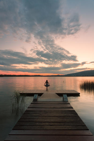 Woman dancing on a Wood pier on Pusiano lake at sunset, Bosisio Parini, Lecco province, Lombardy, italy