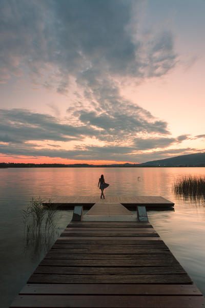 Woman dancing on a Wood pier on Pusiano lake at sunset, Bosisio Parini, Lecco province, Lombardy, italy
