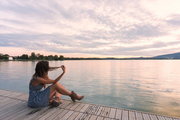 Woman admiring sunset light on Pusiano lake from a wood pier,Bosisio Parini, Lecco province, Lombardy, italy 
