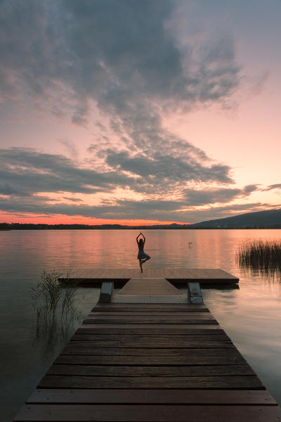 Woman dancing on a Wood pier on Pusiano lake at sunset, Bosisio Parini, Lecco province, Lombardy, italy
