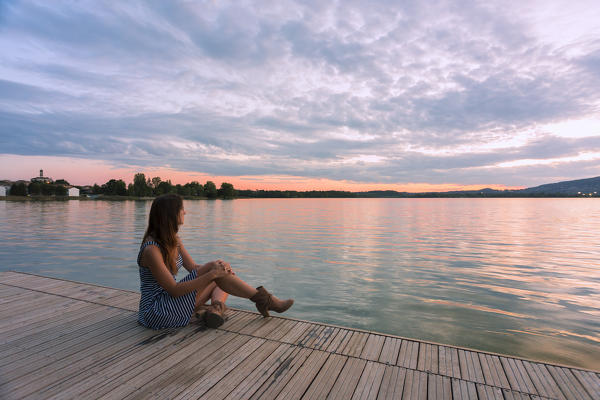 Woman admiring sunset light on Pusiano lake from a wood pier,Bosisio Parini, Lecco province, Lombardy, italy 