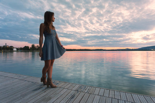 Woman admiring sunset light on Pusiano lake from a wood pier,Bosisio Parini, Lecco province, Lombardy, italy 