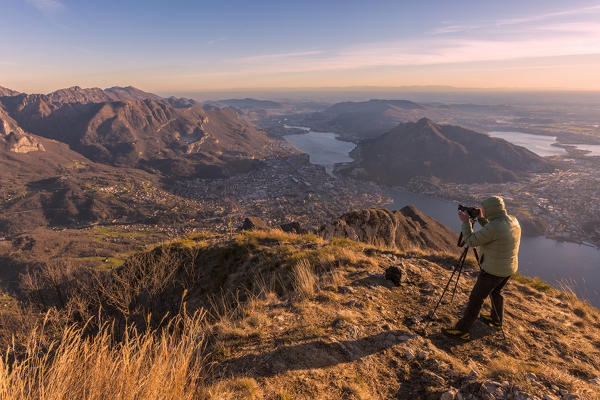 A photographer taking photos of Lecco Lake and Adda river from Coltignone mount at dusk, Lecco Province, lombardy, italy