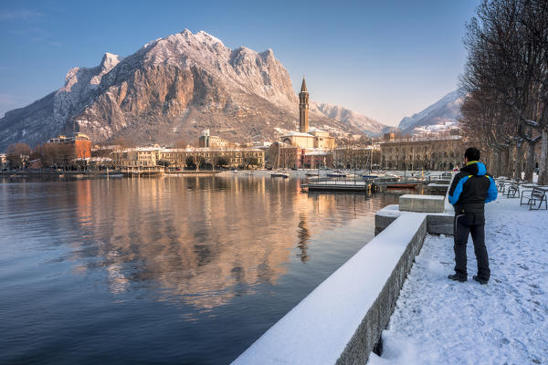 Tourists admiring the snowy lakefront of Lecco and San Martino Mountain reflected in Como lake, Lecco province, Lombardy, Italy