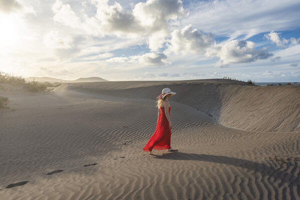 Beautiful girl with red dress walks in the sand dunes of Famara, Lanzarote, Canary Island, Spain, Europe
