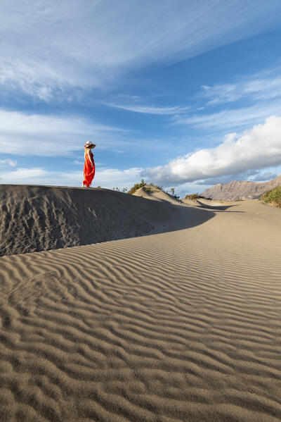 Beautiful girl with red dress walks in the sand dunes of Famara, Lanzarote, Canary Island, Spain, Europe
