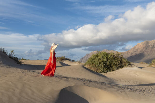 Beautiful girl with red dress walks in the sand dunes of Famara, Lanzarote, Canary Island, Spain, Europe
