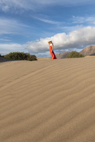 Beautiful girl with red dress walks in the sand dunes of Famara, Lanzarote, Canary Island, Spain, Europe
