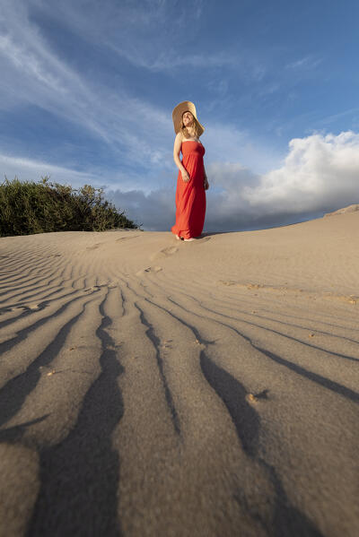 Beautiful girl with red dress walks in the sand dunes of Famara, Lanzarote, Canary Island, Spain, Europe
