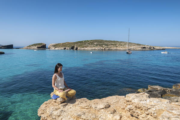 Beautiful girl practices yoga at Blue Lagoon of Comino Island, Malta, Europe
