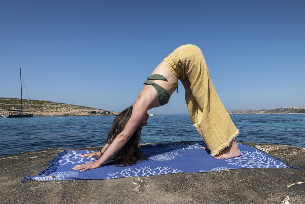 Beautiful girl practices yoga at Blue Lagoon of Comino Island, Malta, Europe