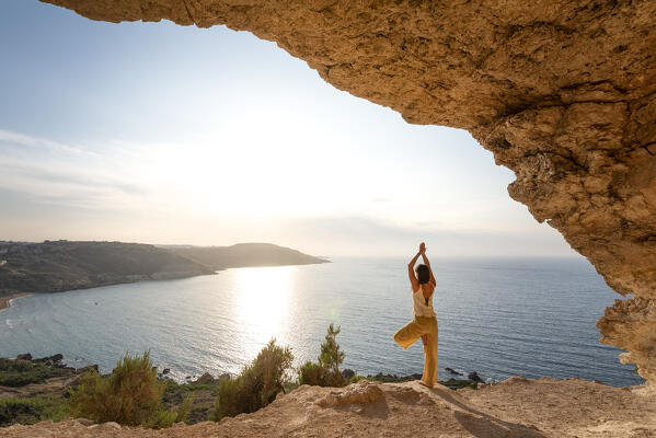 Beautiful girl practices yoga in the cave of Gozo Island during sunset, Malta, Europe (MR)