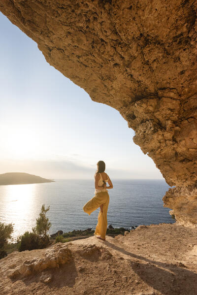 Beautiful girl practices yoga in the cave of Gozo Island during sunset, Malta, Europe (MR)