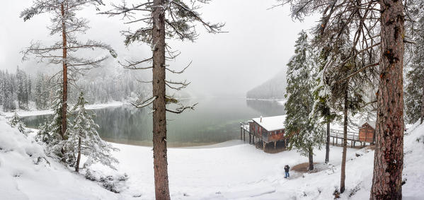 one person admires the splendid and famous Braies Lake under a big snowfall, Natural Park Fanes-Sennes-braies, Dolomiti, municipality of Braies, Bolzano province, Trentino Alto Adige district, Italy, Europe.