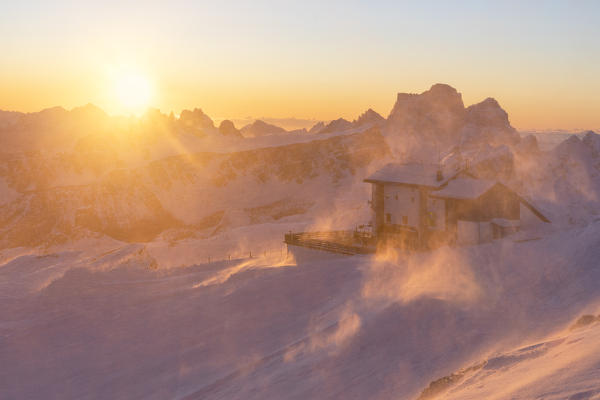 a windstorm lifts the snow in a cold winter sunrise at the Lagazuoi refuge, munipality of Cortina d'Ampezzo, Belluno province, Veneto District, Dolomiti, Italy, Europe