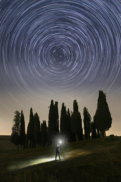 one person observes the rotation of the stars around Polaris, near the iconic Cypresses of San Quirico d'Orcia, Siena province, Tuscany district, Italy, Europe