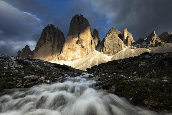 a warm light filters through the clouds and envelops the Tre Cime di Lavaredo during a summer sunset, Dolomiti, municipality of Dobbiaco, Bolzano province, Veneto district, Italy Europe