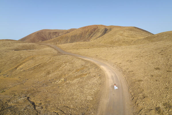 aerial view taken by drone of the volcanic area near to Corralejo during a summer sunset with a girl along the road, Natural Park of Corralejo, Fuerteventura, Canary Island, Spain, Europe