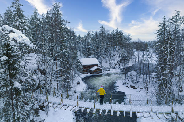 A woman observin the landscape from the suspended bridge with the mill of Myllykoski in background, Juuma, Oulanka National Park, Kuusamo, Lapland, Finland